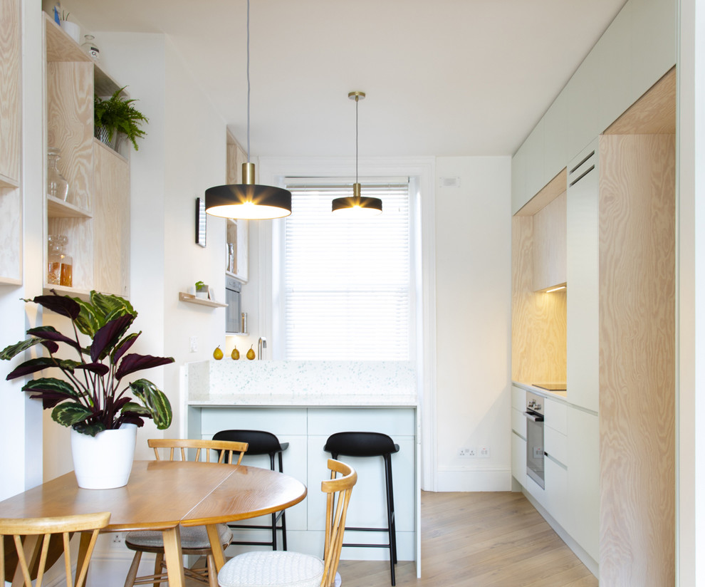 Small scandinavian open plan kitchen in London with a single-bowl sink, flat-panel cabinets, recycled glass benchtops, white splashback, stainless steel appliances, medium hardwood floors, with island and white benchtop.