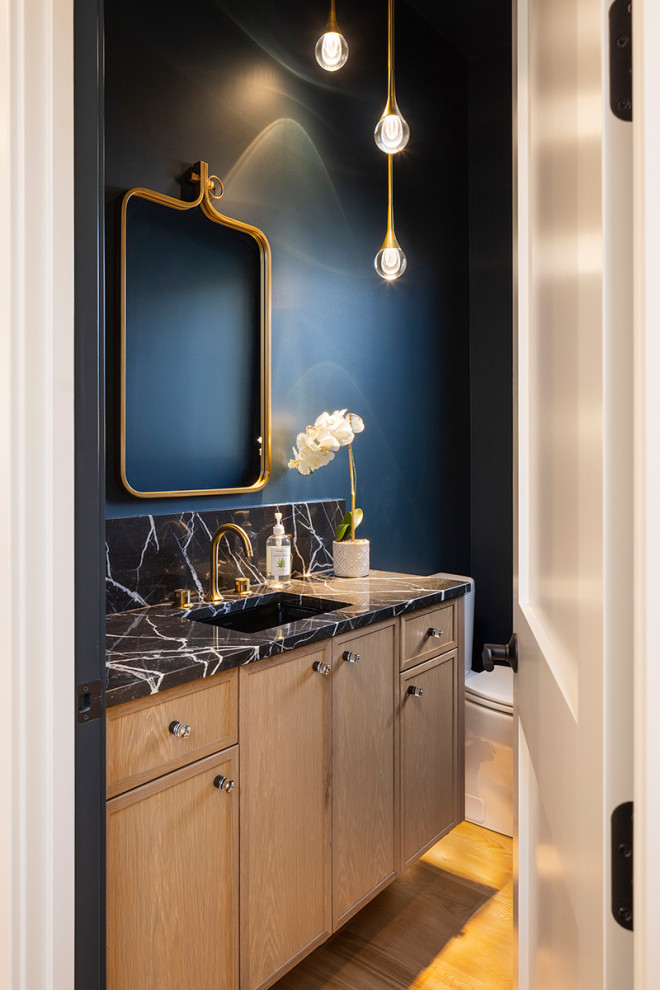 Photo of a small modern cloakroom in Minneapolis with recessed-panel cabinets, light wood cabinets, a one-piece toilet, blue walls, medium hardwood flooring, a submerged sink, granite worktops, brown floors, black worktops and a floating vanity unit.