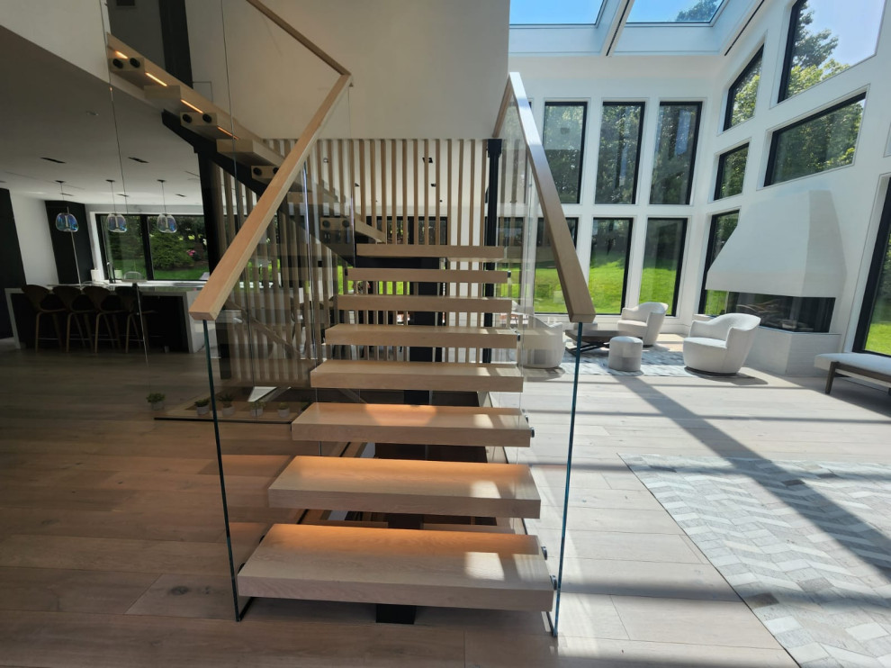 Источник вдохновения для домашнего уюта: огромная угловая металлическая лестница в современном стиле с деревянными ступенями, стеклянными перилами и панелями на части стены