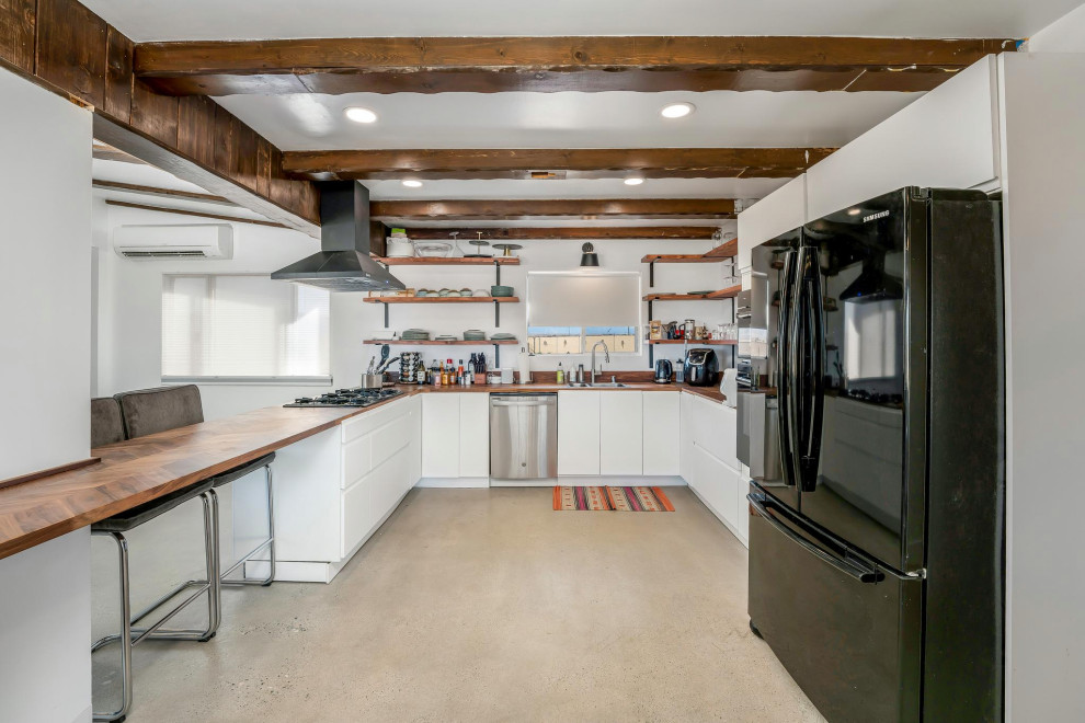 Inredning av ett modernt litet brun brunt kök, med släta luckor, en halv köksö, en dubbel diskho, vita skåp, träbänkskiva, rostfria vitvaror, betonggolv och beiget golv