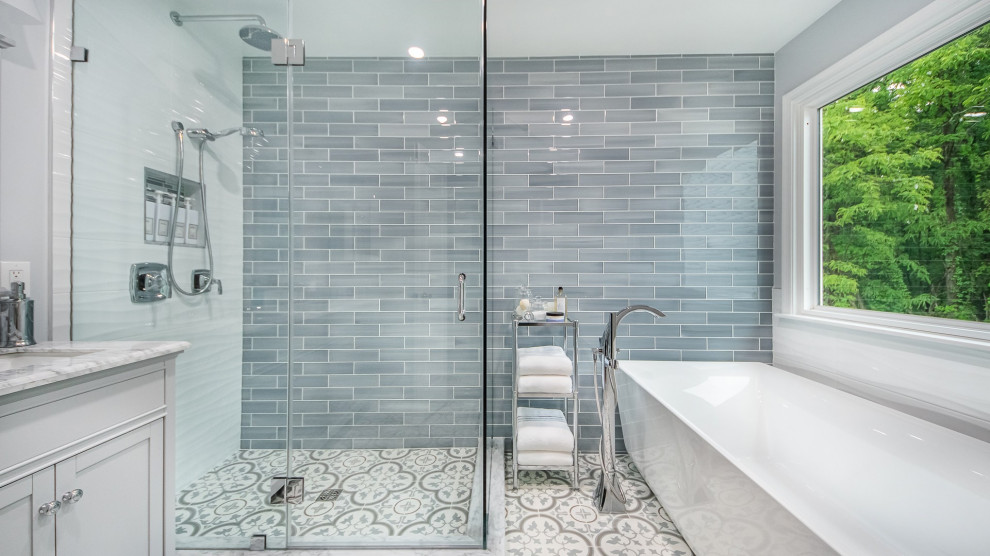 Inspiration for a mid-sized transitional master bathroom in DC Metro with shaker cabinets, white cabinets, a freestanding tub, an alcove shower, a one-piece toilet, multi-coloured tile, glass tile, multi-coloured walls, ceramic floors, an undermount sink, engineered quartz benchtops, multi-coloured floor, a hinged shower door, grey benchtops, a niche, a double vanity and a freestanding vanity.
