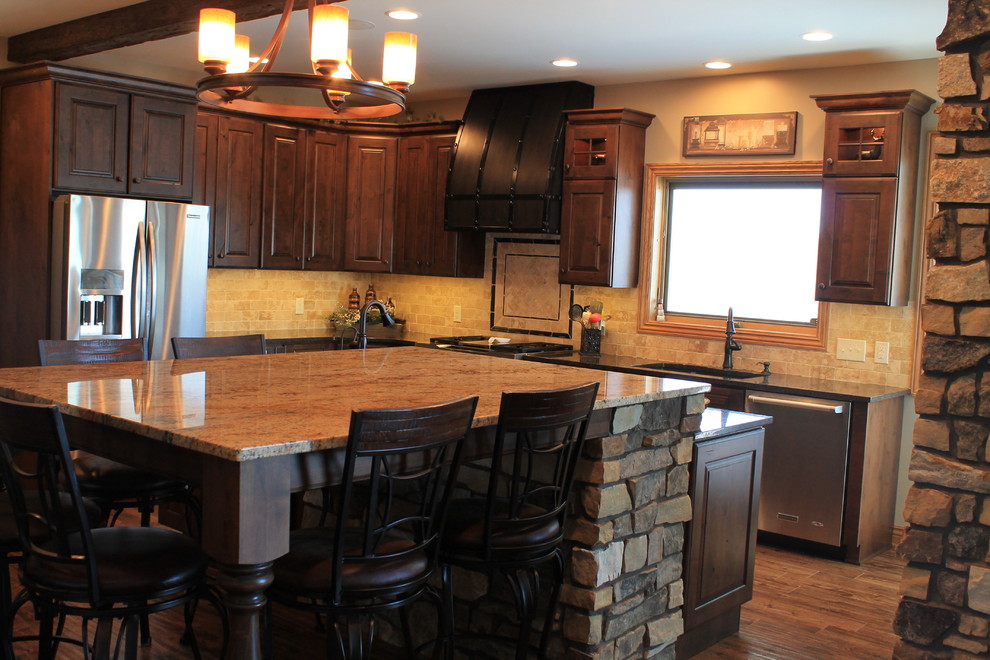 Example of a mid-sized mountain style u-shaped medium tone wood floor kitchen design with raised-panel cabinets, dark wood cabinets, granite countertops, beige backsplash, ceramic backsplash, black appliances and an island
