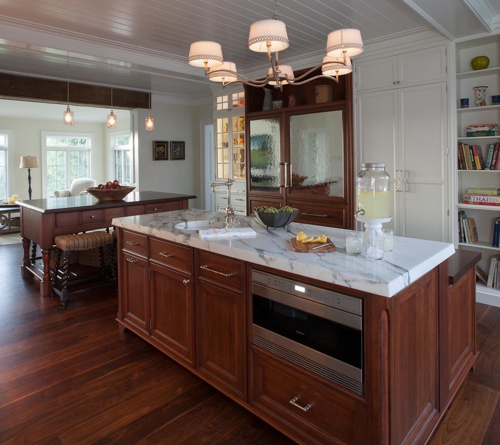 Photo of a country u-shaped open plan kitchen in DC Metro with recessed-panel cabinets, medium wood cabinets, panelled appliances, a farmhouse sink, marble benchtops, multi-coloured splashback, stone slab splashback, dark hardwood floors and multiple islands.