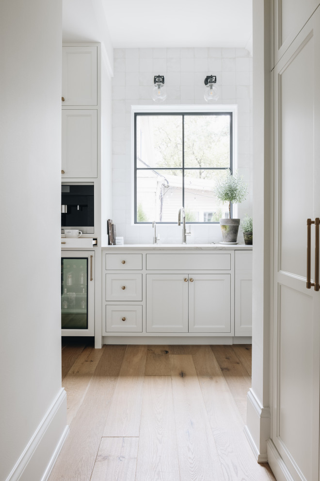 Inspiration for a large transitional kitchen pantry in Chicago with a drop-in sink, shaker cabinets, white cabinets, white splashback, light hardwood floors, brown floor and multi-coloured benchtop.