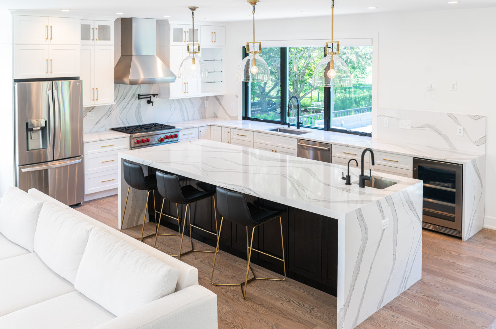 Classic kitchen/diner in New York with shaker cabinets, white cabinets, marble worktops, white splashback, marble splashback, stainless steel appliances, an island, brown floors and white worktops.