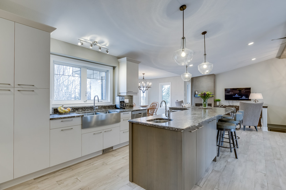 Example of a large transitional l-shaped light wood floor eat-in kitchen design with flat-panel cabinets, white cabinets, gray backsplash, subway tile backsplash, an island and stainless steel appliances