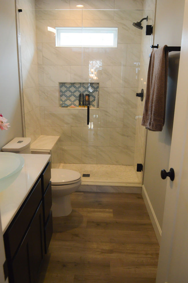 This is an example of a large modern master bathroom in Cincinnati with shaker cabinets, dark wood cabinets, a drop-in tub, an alcove shower, a one-piece toilet, white tile, porcelain tile, grey walls, vinyl floors, a vessel sink, marble benchtops, grey floor, a hinged shower door and white benchtops.