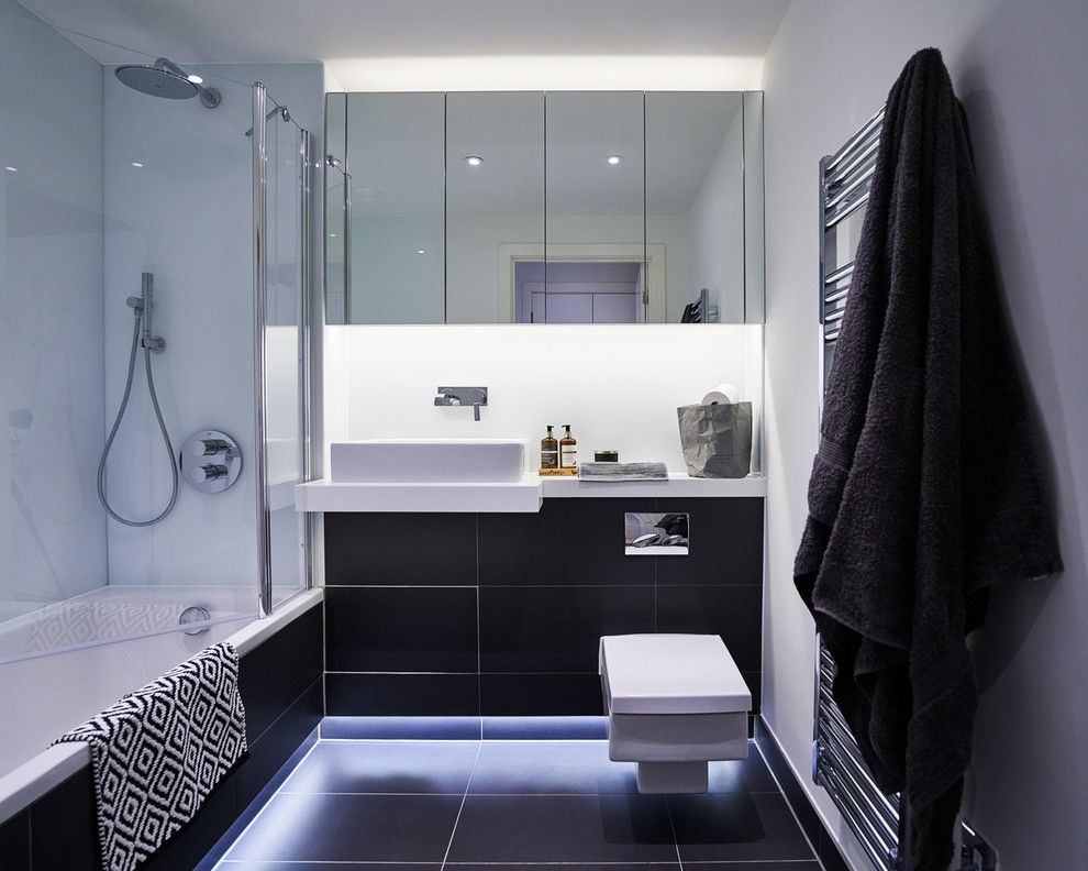 Design ideas for a contemporary bathroom in London with flat-panel cabinets, black cabinets, a drop-in tub, a shower/bathtub combo, a wall-mount toilet, black tile, white walls and a vessel sink.