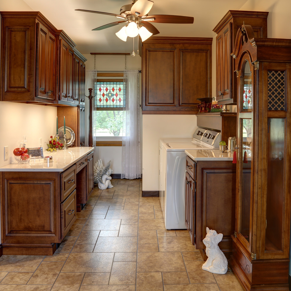 Mid-sized traditional galley utility room in Other with raised-panel cabinets, dark wood cabinets, marble benchtops, beige walls, ceramic floors and a side-by-side washer and dryer.