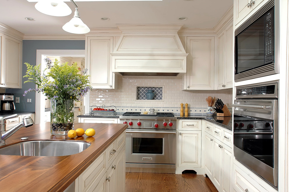 Inspiration for a mid-sized traditional kitchen in Chicago with stainless steel appliances, wood benchtops, an undermount sink, raised-panel cabinets, white splashback and subway tile splashback.