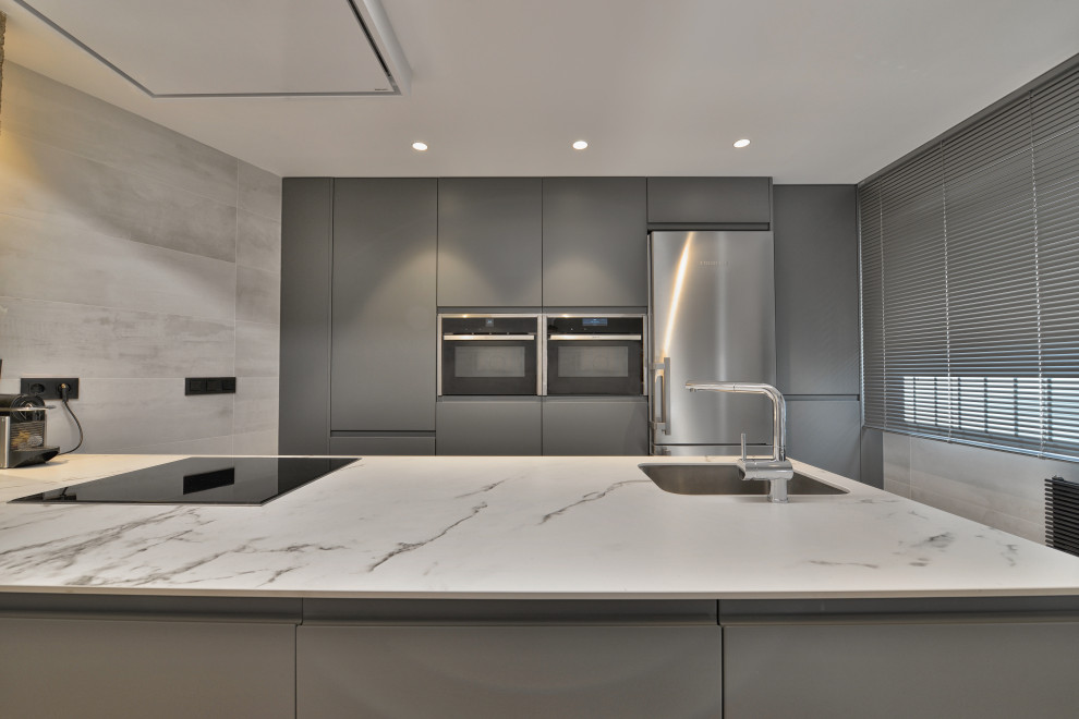 Design ideas for a mid-sized industrial galley open plan kitchen in Madrid with an undermount sink, flat-panel cabinets, grey cabinets, limestone benchtops, stainless steel appliances, laminate floors, a peninsula, beige floor and white benchtop.