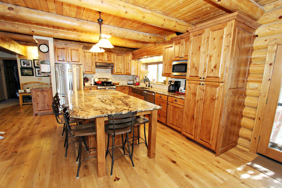 Inspiration for a mid-sized rustic l-shaped light wood floor open concept kitchen remodel with a farmhouse sink, raised-panel cabinets, medium tone wood cabinets, granite countertops, beige backsplash, stone tile backsplash, stainless steel appliances, an island and brown countertops