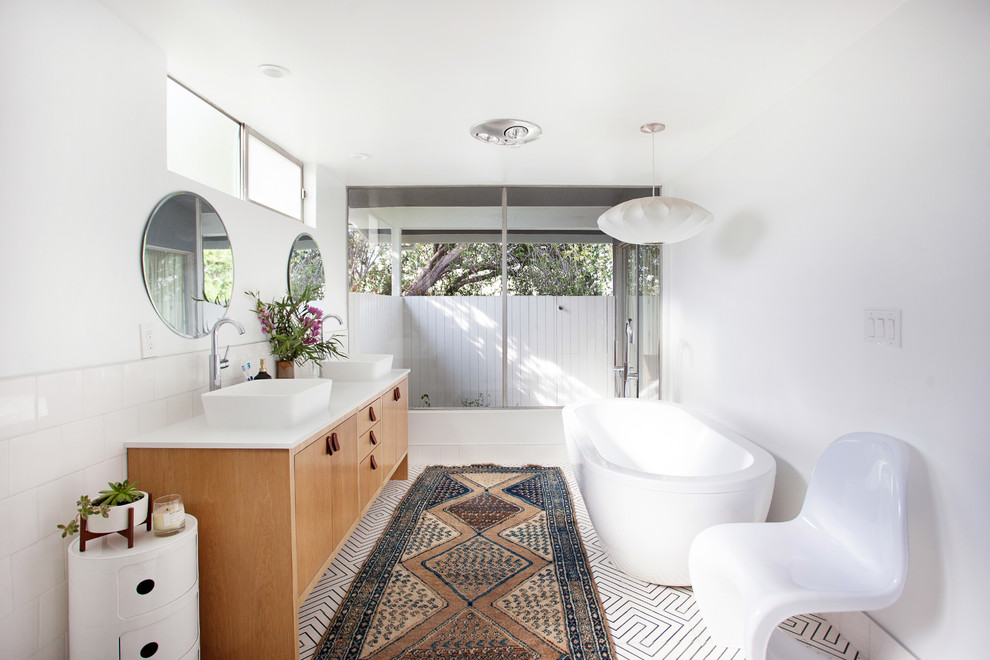 This is an example of a midcentury master bathroom in Los Angeles with flat-panel cabinets, medium wood cabinets, a freestanding tub, white tile, white walls, a vessel sink and white floor.