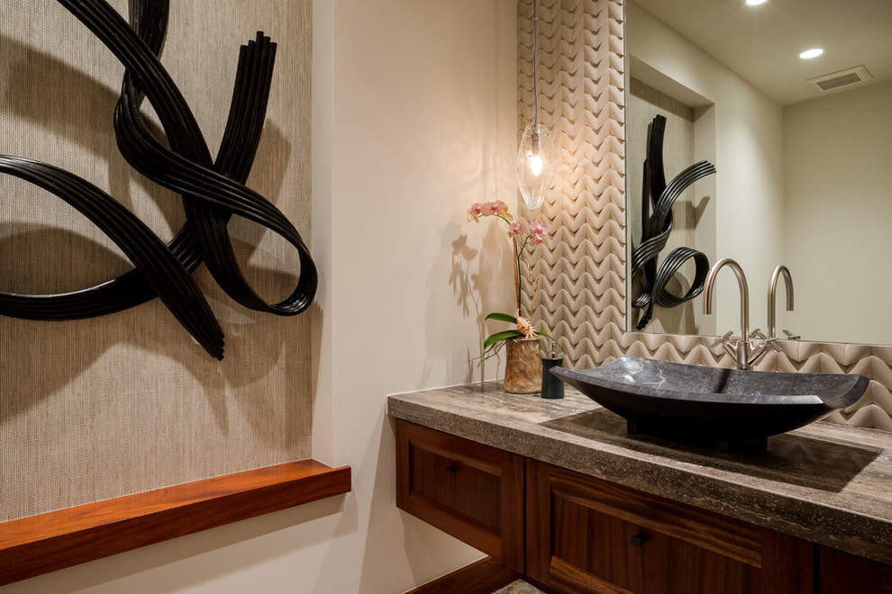 This is an example of a tropical powder room in Hawaii with recessed-panel cabinets, medium wood cabinets, a one-piece toilet, mosaic tile, pebble tile floors, a vessel sink and travertine benchtops.