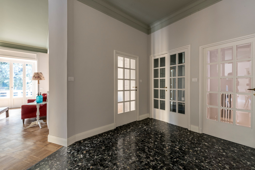 ミラノにある高級な広いトラディショナルスタイルのおしゃれな玄関ロビー (白い壁、大理石の床、白いドア、黒い床、グレーの天井) の写真