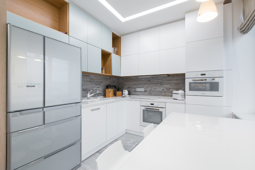 Photo of a mid-sized contemporary l-shaped open plan kitchen in Moscow with an undermount sink, flat-panel cabinets, white cabinets, quartz benchtops, grey splashback, porcelain splashback, white appliances, porcelain floors and no island.