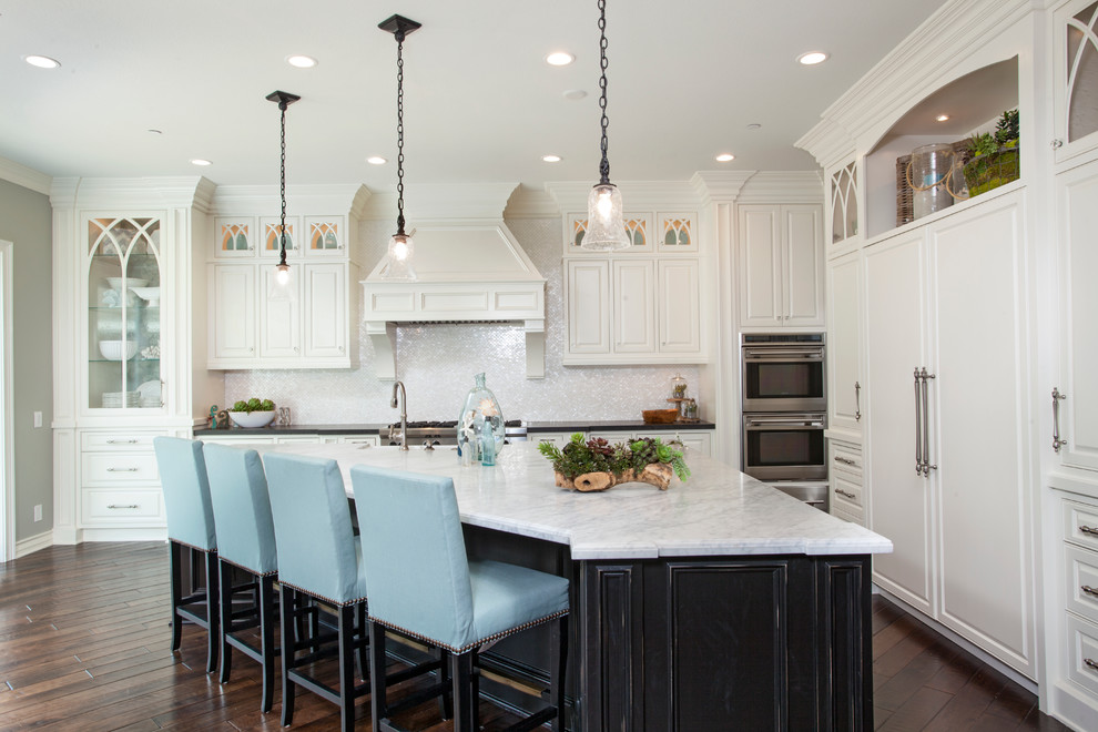 Inspiration for a traditional l-shaped kitchen in Orange County with a farmhouse sink, raised-panel cabinets, white cabinets, white splashback, mosaic tile splashback, panelled appliances, dark hardwood floors and with island.
