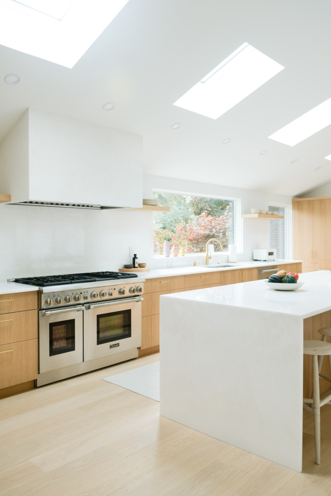 L-shaped open plan kitchen in Detroit with a double-bowl sink, flat-panel cabinets, light wood cabinets, marble benchtops, white splashback, marble splashback, stainless steel appliances, light hardwood floors, with island, beige floor, white benchtop and vaulted.