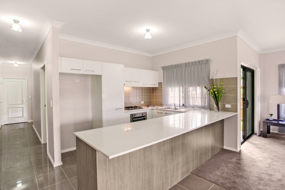 Photo of a small transitional u-shaped open plan kitchen in Newcastle - Maitland with a double-bowl sink, flat-panel cabinets, white cabinets, granite benchtops, beige splashback, ceramic splashback, stainless steel appliances, porcelain floors, a peninsula and grey floor.