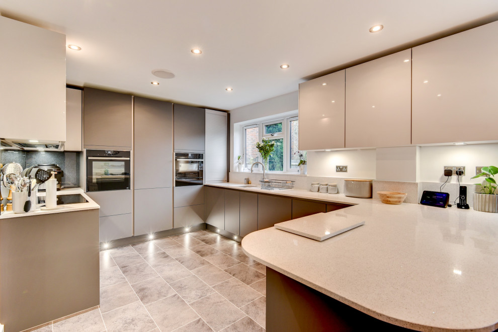 This is an example of a large modern u-shaped open plan kitchen in Sussex with an undermount sink, flat-panel cabinets, grey cabinets, quartzite benchtops, grey splashback, glass sheet splashback, panelled appliances, vinyl floors, a peninsula, grey floor and white benchtop.