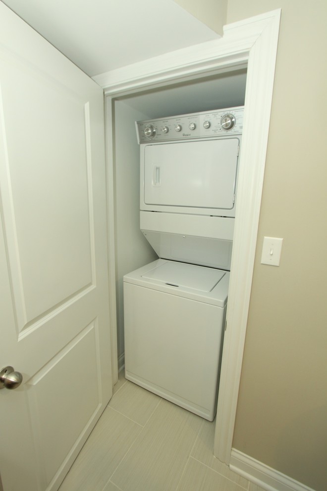 Photo of a small modern single-wall laundry cupboard in Chicago with beige walls, porcelain floors, a stacked washer and dryer and grey floor.