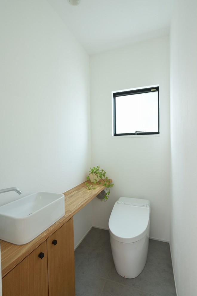 This is an example of a mid-sized contemporary powder room in Other with furniture-like cabinets, white tile, white walls and grey floor.