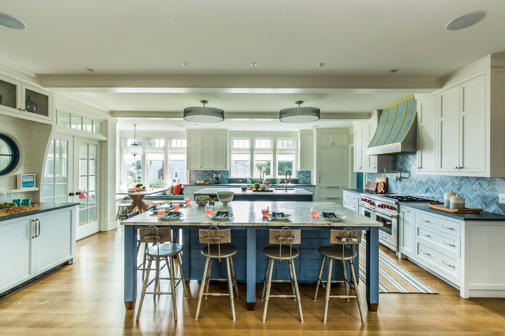 This is an example of an expansive beach style u-shaped eat-in kitchen in Bridgeport with an undermount sink, shaker cabinets, white cabinets, blue splashback, panelled appliances, medium hardwood floors, multiple islands, brown floor and multi-coloured benchtop.