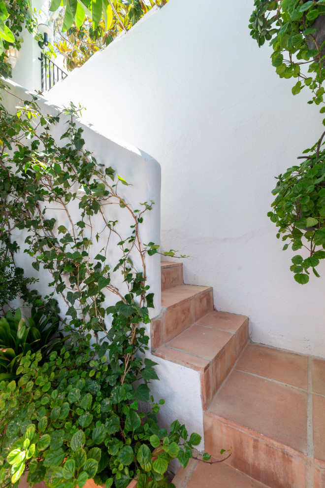 Cette image montre un petit escalier méditerranéen avec des marches en terre cuite, des contremarches en terre cuite et un garde-corps en matériaux mixtes.