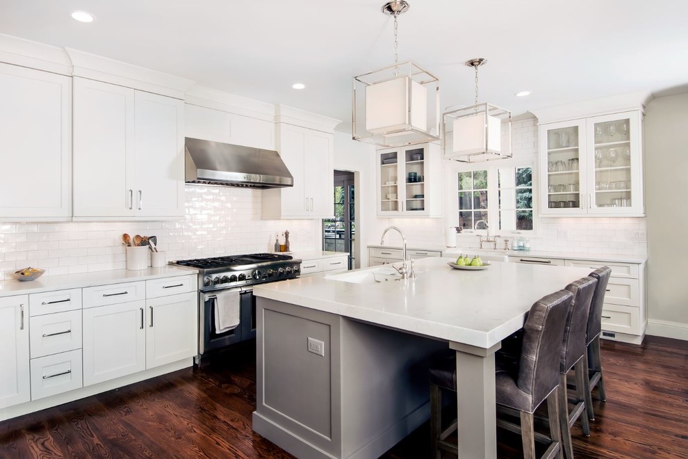 Transitional l-shaped kitchen in Denver with a farmhouse sink, shaker cabinets, white cabinets, white splashback, subway tile splashback, stainless steel appliances, medium hardwood floors, with island and brown floor.