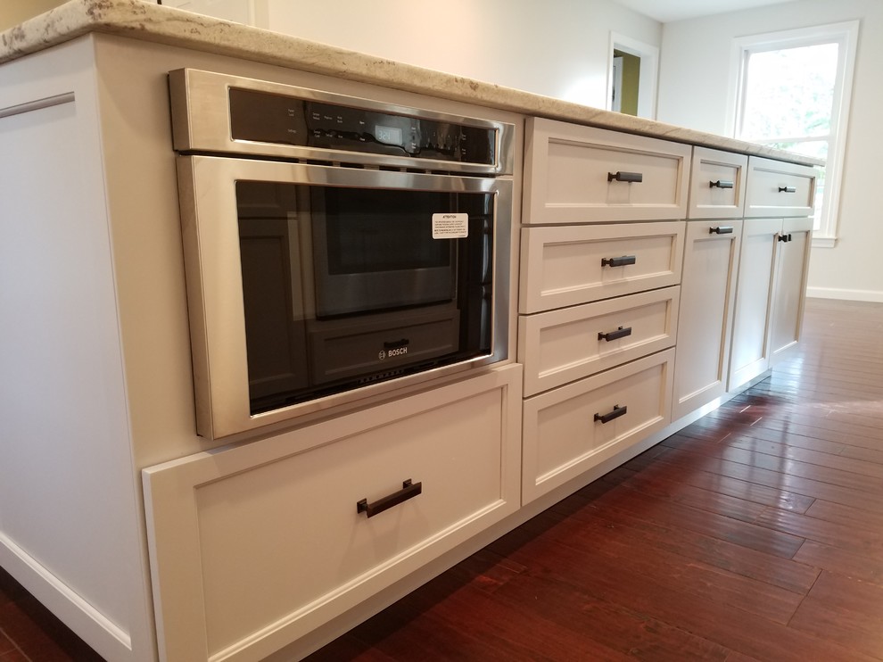 Eat-in kitchen - mid-sized transitional l-shaped dark wood floor and brown floor eat-in kitchen idea with a farmhouse sink, shaker cabinets, white cabinets, granite countertops, white backsplash, subway tile backsplash, stainless steel appliances and an island