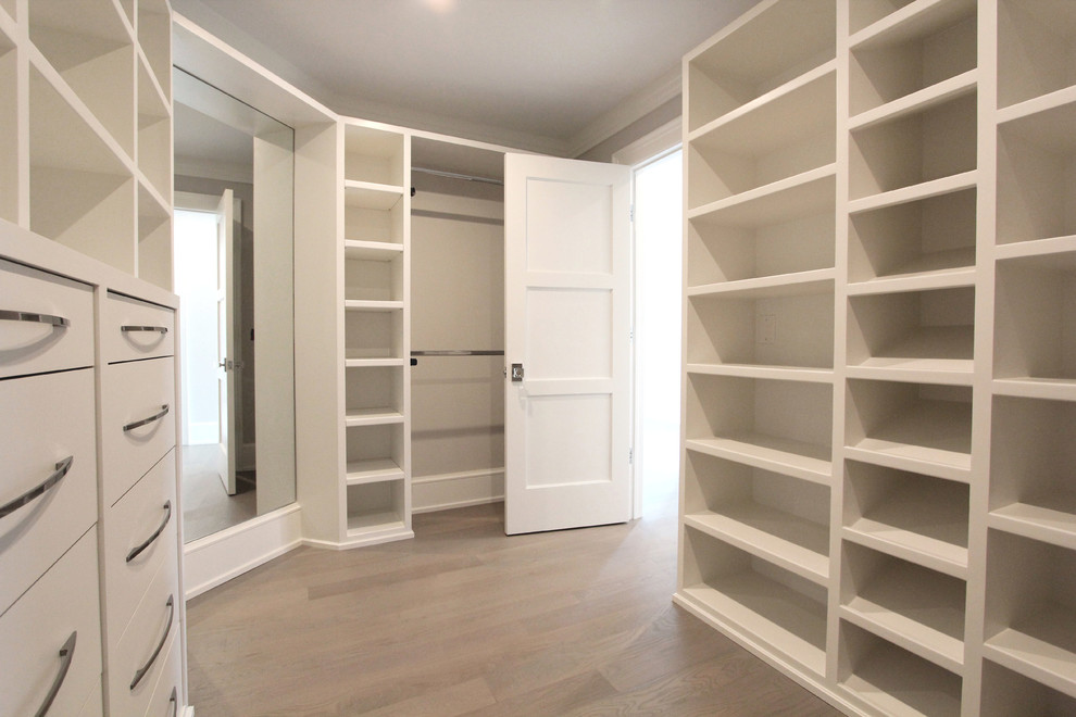 Large contemporary gender-neutral walk-in wardrobe in New York with open cabinets, white cabinets, light hardwood floors and beige floor.