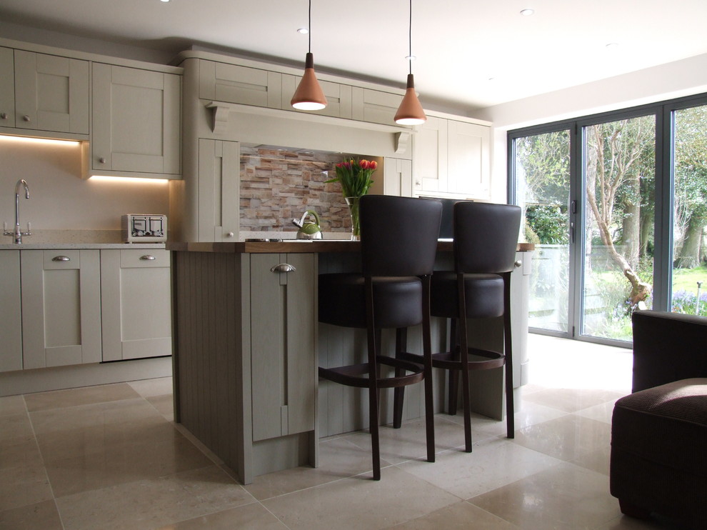 Photo of a mid-sized modern single-wall open plan kitchen in Hampshire with a drop-in sink, shaker cabinets, beige cabinets, quartzite benchtops, multi-coloured splashback, glass sheet splashback, black appliances, travertine floors and with island.