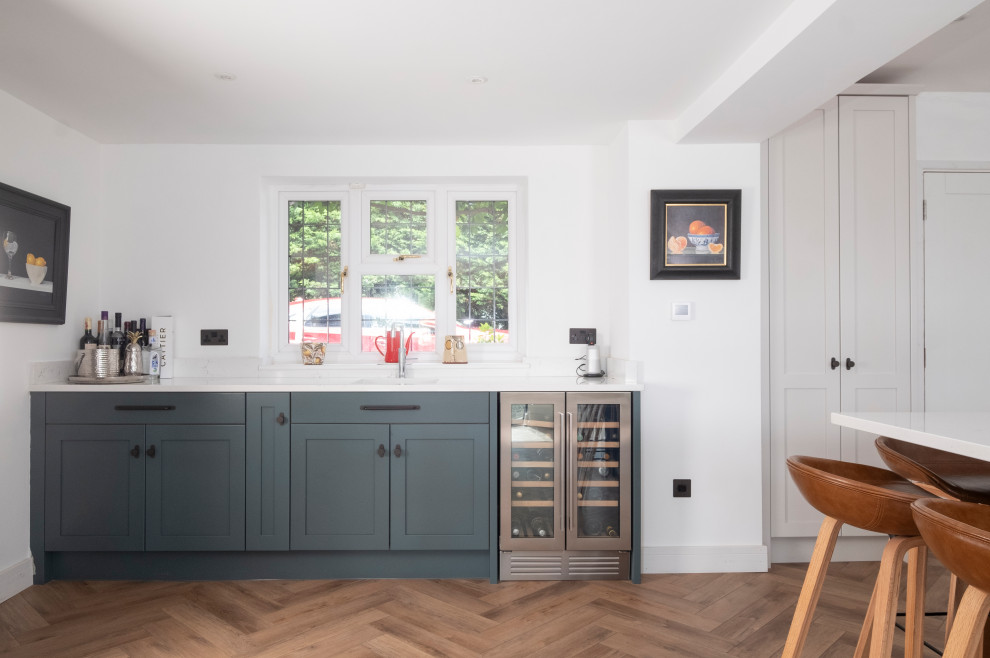 Large classic l-shaped kitchen in Cardiff with an integrated sink, shaker cabinets, light wood cabinets, quartz worktops, stainless steel appliances, laminate floors, an island and white worktops.