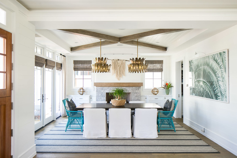 Inspiration for a large tropical dining room in Los Angeles with white walls, medium hardwood floors, a standard fireplace, a stone fireplace surround and brown floor.