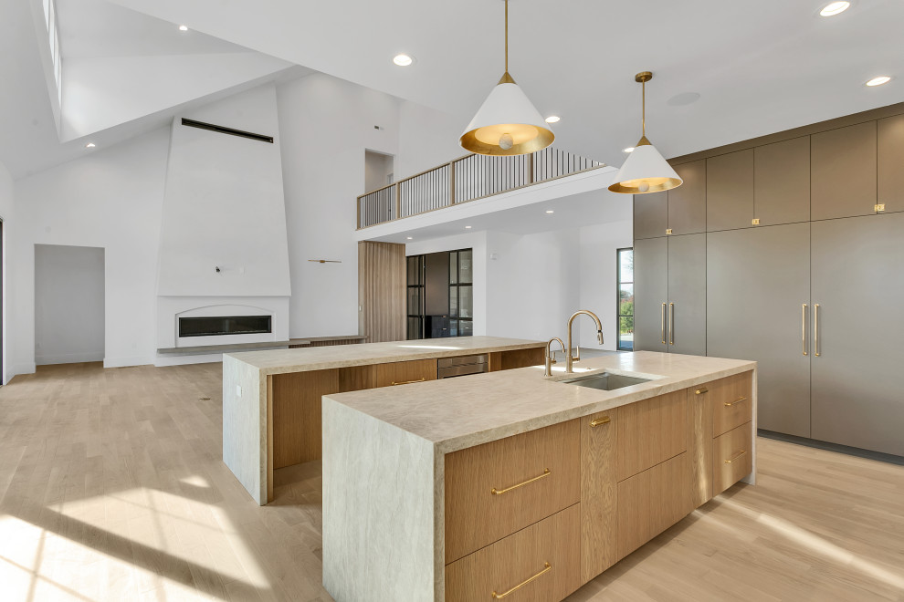 Large transitional u-shaped light wood floor, beige floor and vaulted ceiling open concept kitchen photo with an undermount sink, flat-panel cabinets, light wood cabinets, quartzite countertops, white backsplash, paneled appliances, two islands and beige countertops