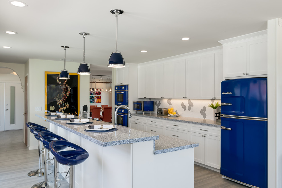 Photo of a large transitional single-wall eat-in kitchen in San Diego with an undermount sink, raised-panel cabinets, white cabinets, granite benchtops, multi-coloured splashback, ceramic splashback, coloured appliances, porcelain floors, with island, beige floor and blue benchtop.