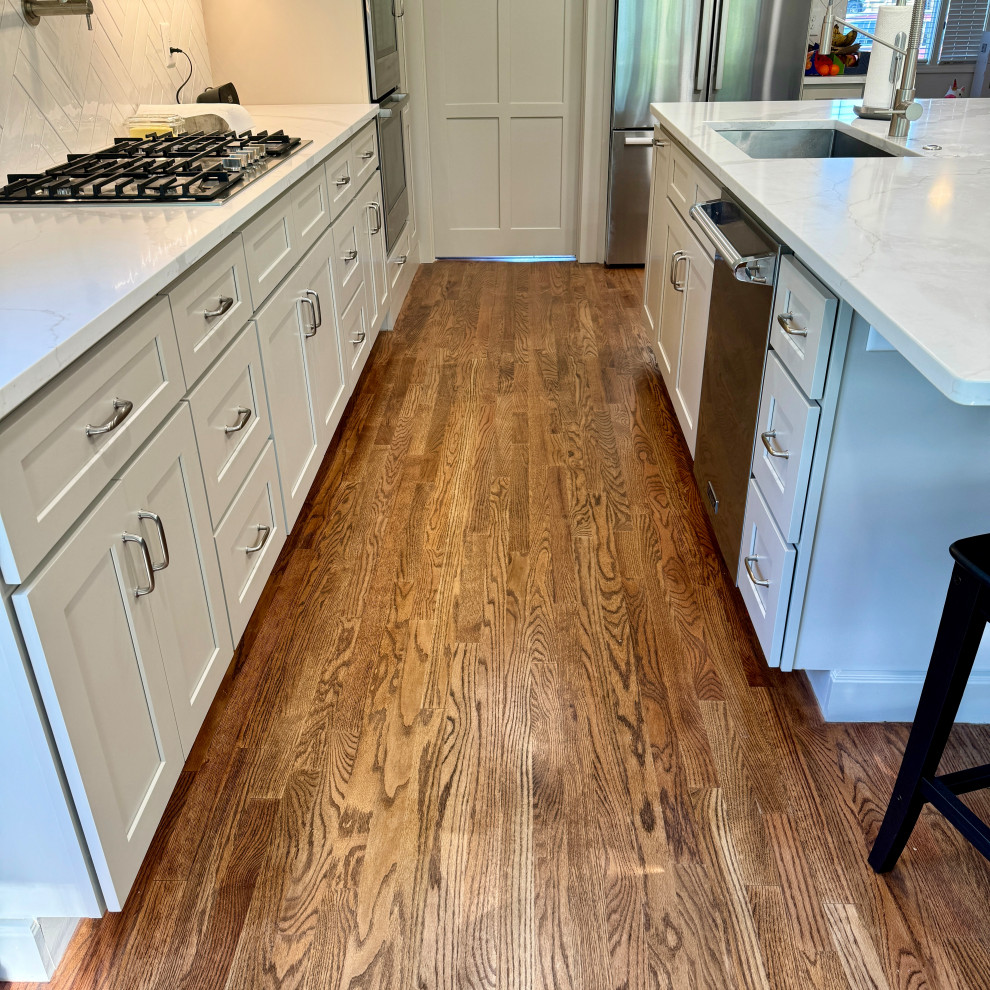 Example of a mid-sized transitional l-shaped medium tone wood floor, brown floor and wallpaper ceiling eat-in kitchen design in Atlanta with an undermount sink, shaker cabinets, white cabinets, granite countertops, white backsplash, stainless steel appliances, an island and white countertops
