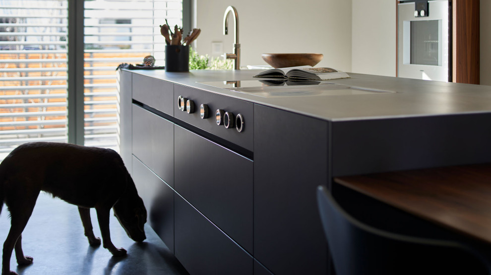 Contemporary open plan kitchen in Munich with black cabinets, black splashback, concrete floors and with island.