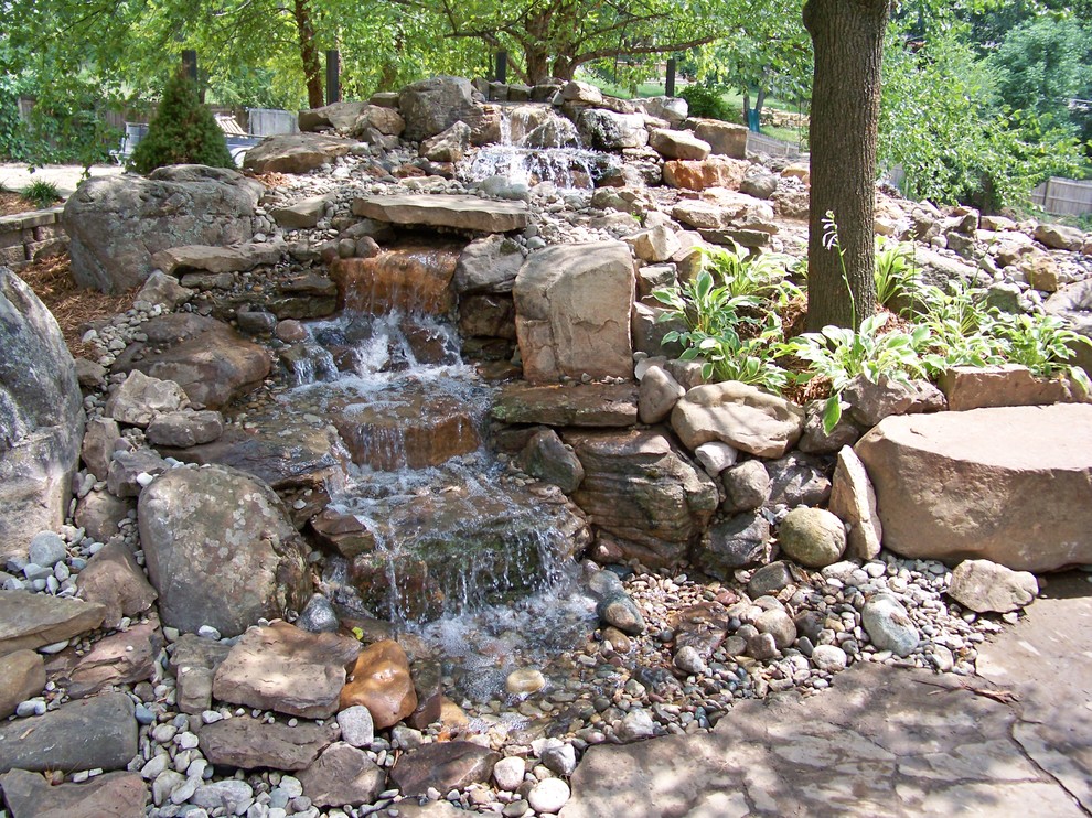 This is an example of a mid-sized tropical front yard shaded garden for summer in Kansas City with a water feature and gravel.