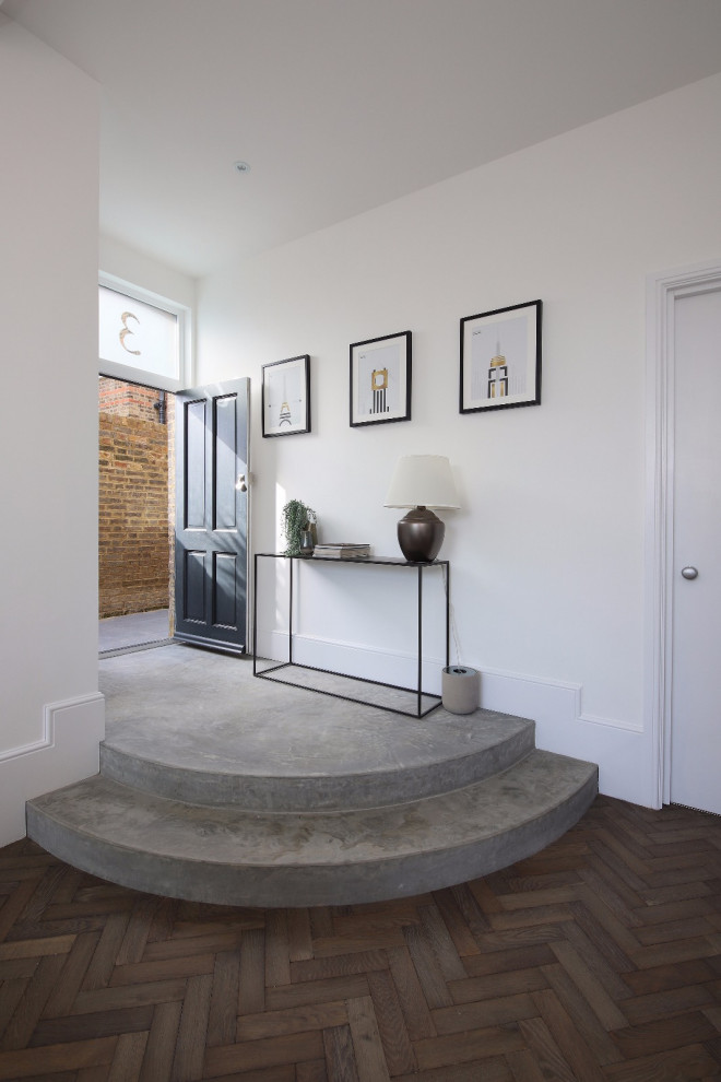 Photo of a mid-sized contemporary entry hall in London with white walls, medium hardwood floors, a single front door, a black front door and brown floor.