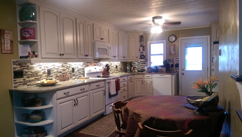 Inspiration for a mid-sized transitional l-shaped laminate floor eat-in kitchen remodel with an undermount sink, raised-panel cabinets, white cabinets, granite countertops, multicolored backsplash, mosaic tile backsplash, white appliances and no island
