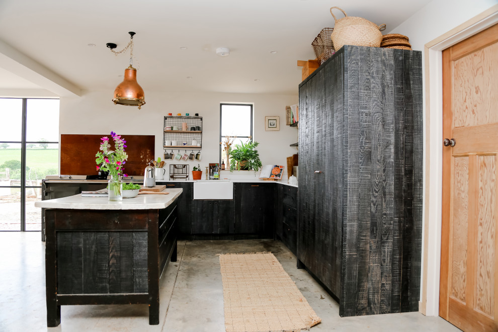 Inspiration for a medium sized industrial l-shaped kitchen in Other with flat-panel cabinets, quartz worktops, white worktops, a belfast sink, black cabinets, integrated appliances, concrete flooring, an island and grey floors.