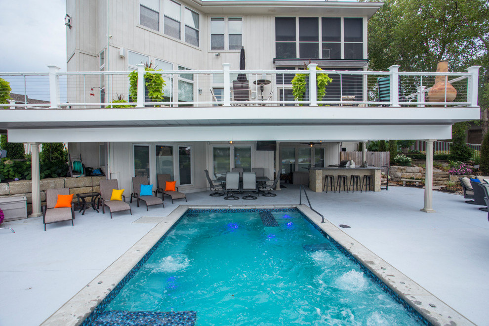 Foto di un'ampia piscina monocorsia classica rettangolare dietro casa con una vasca idromassaggio e lastre di cemento
