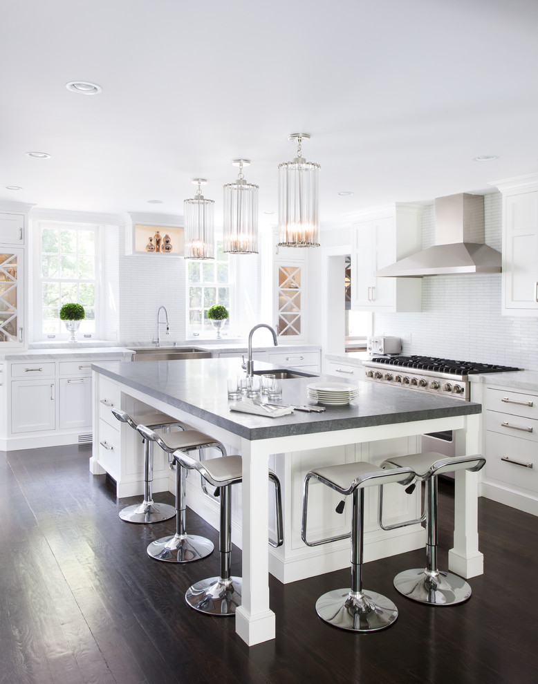 Photo of a large transitional l-shaped open plan kitchen in New York with a farmhouse sink, recessed-panel cabinets, white cabinets, white splashback, quartz benchtops, ceramic splashback, stainless steel appliances, dark hardwood floors and with island.