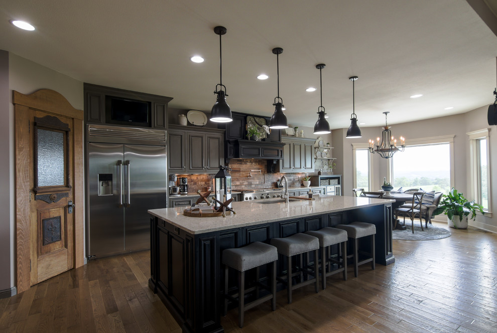 Large transitional single-wall medium tone wood floor and brown floor eat-in kitchen photo with an undermount sink, raised-panel cabinets, gray cabinets, multicolored backsplash, stainless steel appliances, an island, beige countertops and stone tile backsplash