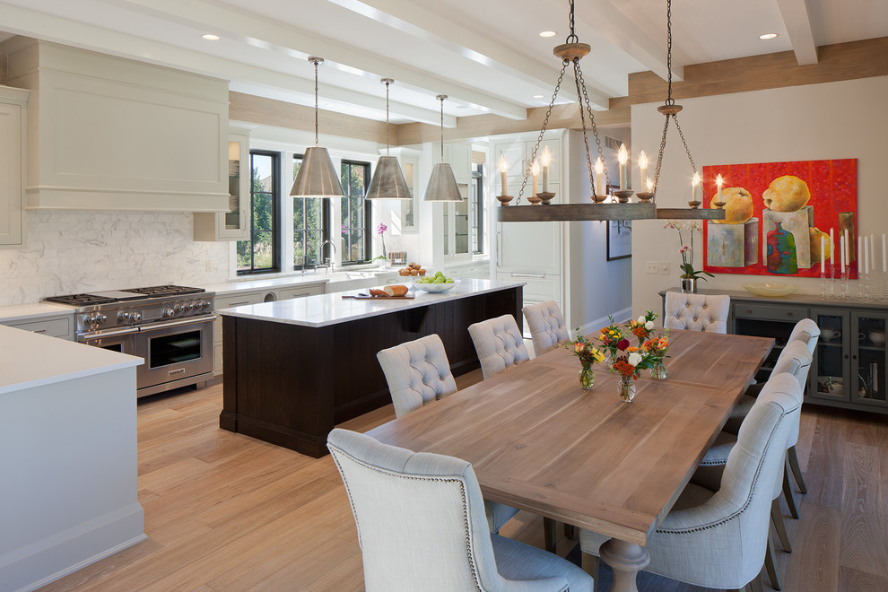 This is an example of a large transitional l-shaped eat-in kitchen in Grand Rapids with a farmhouse sink, recessed-panel cabinets, white cabinets, white splashback, subway tile splashback, stainless steel appliances, quartz benchtops, light hardwood floors, with island and brown floor.