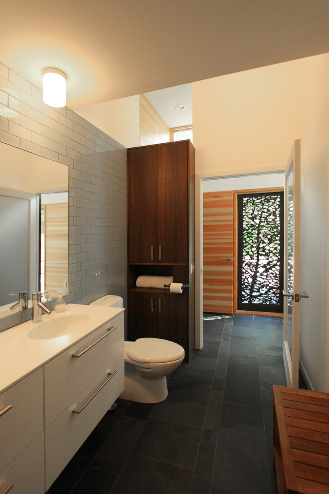 Inspiration for a mid-sized contemporary bathroom in Minneapolis with an integrated sink, flat-panel cabinets, white cabinets, a two-piece toilet, white tile, subway tile, white walls and slate floors.