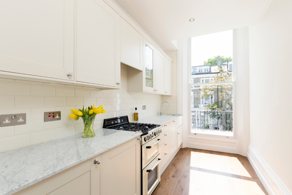 Inspiration for a small country separate kitchen in London with shaker cabinets, white cabinets, white splashback, subway tile splashback, stainless steel appliances and medium hardwood floors.