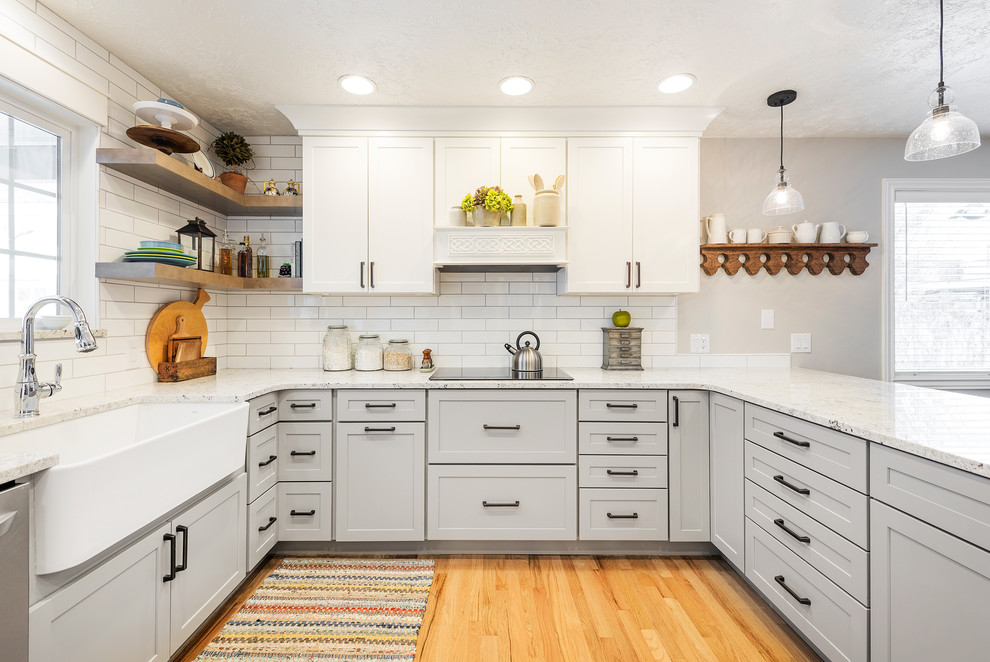 Design ideas for a country u-shaped kitchen in Salt Lake City with a farmhouse sink, shaker cabinets, grey cabinets, white splashback, subway tile splashback, medium hardwood floors, a peninsula, brown floor and white benchtop.