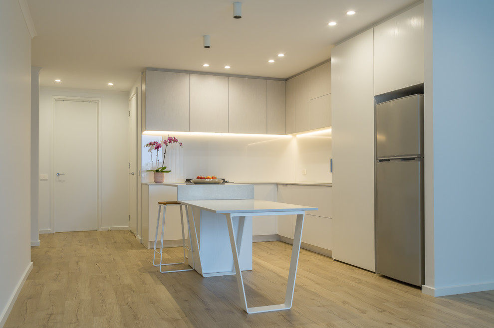 Inspiration for a mid-sized modern l-shaped open plan kitchen in Melbourne with an undermount sink, open cabinets, white cabinets, quartz benchtops, white splashback, glass sheet splashback, black appliances, laminate floors, with island, beige floor and grey benchtop.